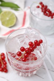 Refreshing water with red currants in glass on light table, closeup