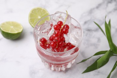 Photo of Refreshing water with red currants in glass on white marble table, closeup