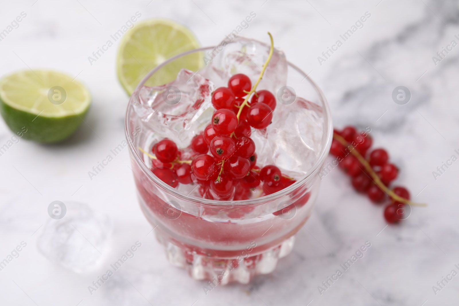 Photo of Refreshing water with red currants in glass on white marble table, closeup