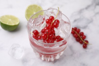 Refreshing water with red currants in glass on white marble table, closeup