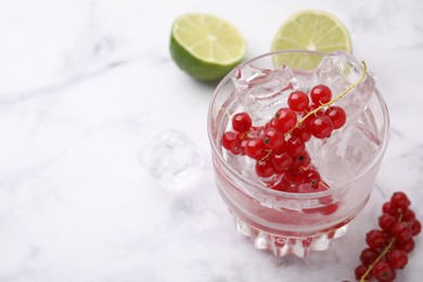 Refreshing water with red currants in glass on white marble table, closeup. Space for text