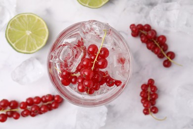 Photo of Refreshing water with red currants in glass on white marble table, flat lay