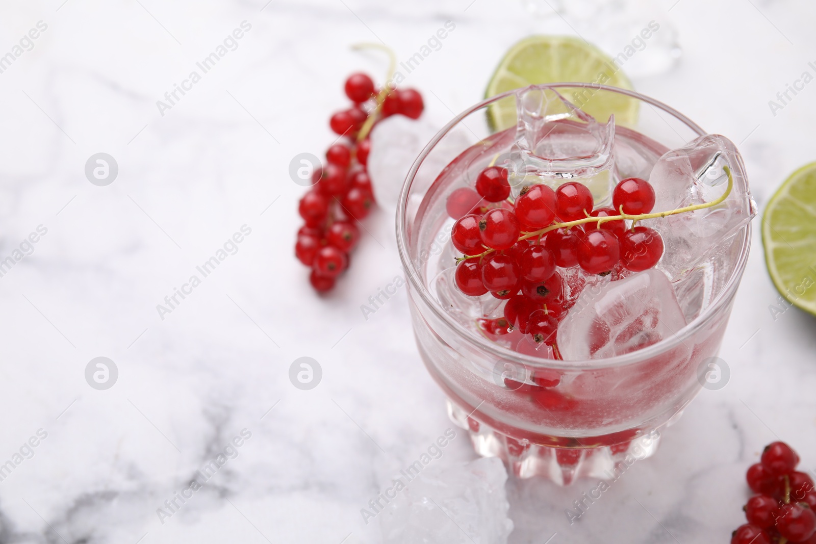 Photo of Refreshing water with red currants in glass on white marble table, closeup. Space for text