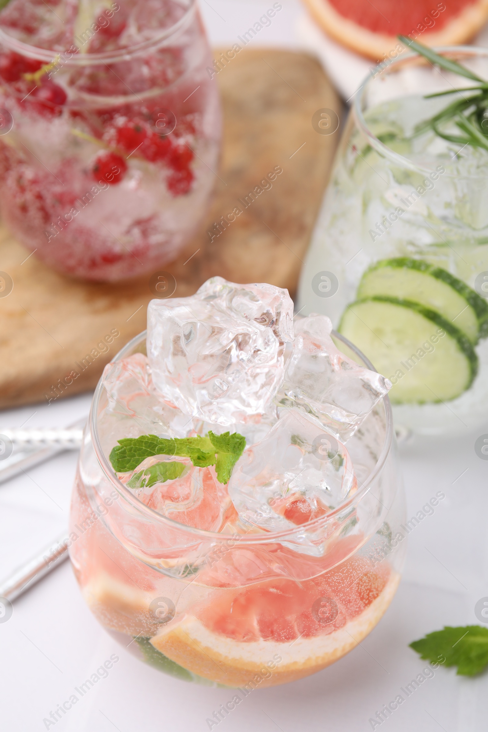 Photo of Different refreshing drinks in glasses on white tiled table, closeup