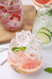 Different refreshing drinks in glasses on white tiled table, closeup