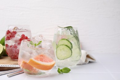 Photo of Different refreshing drinks in glasses on white tiled table, space for text