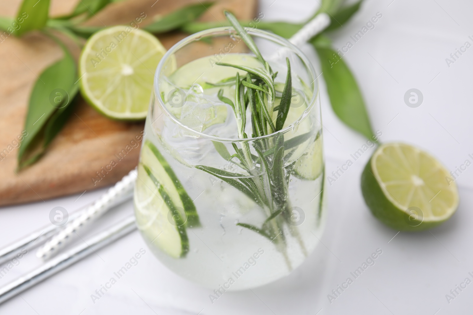 Photo of Refreshing water with cucumber and rosemary in glass on white tiled table, closeup