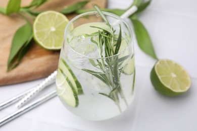 Refreshing water with cucumber and rosemary in glass on white tiled table, closeup