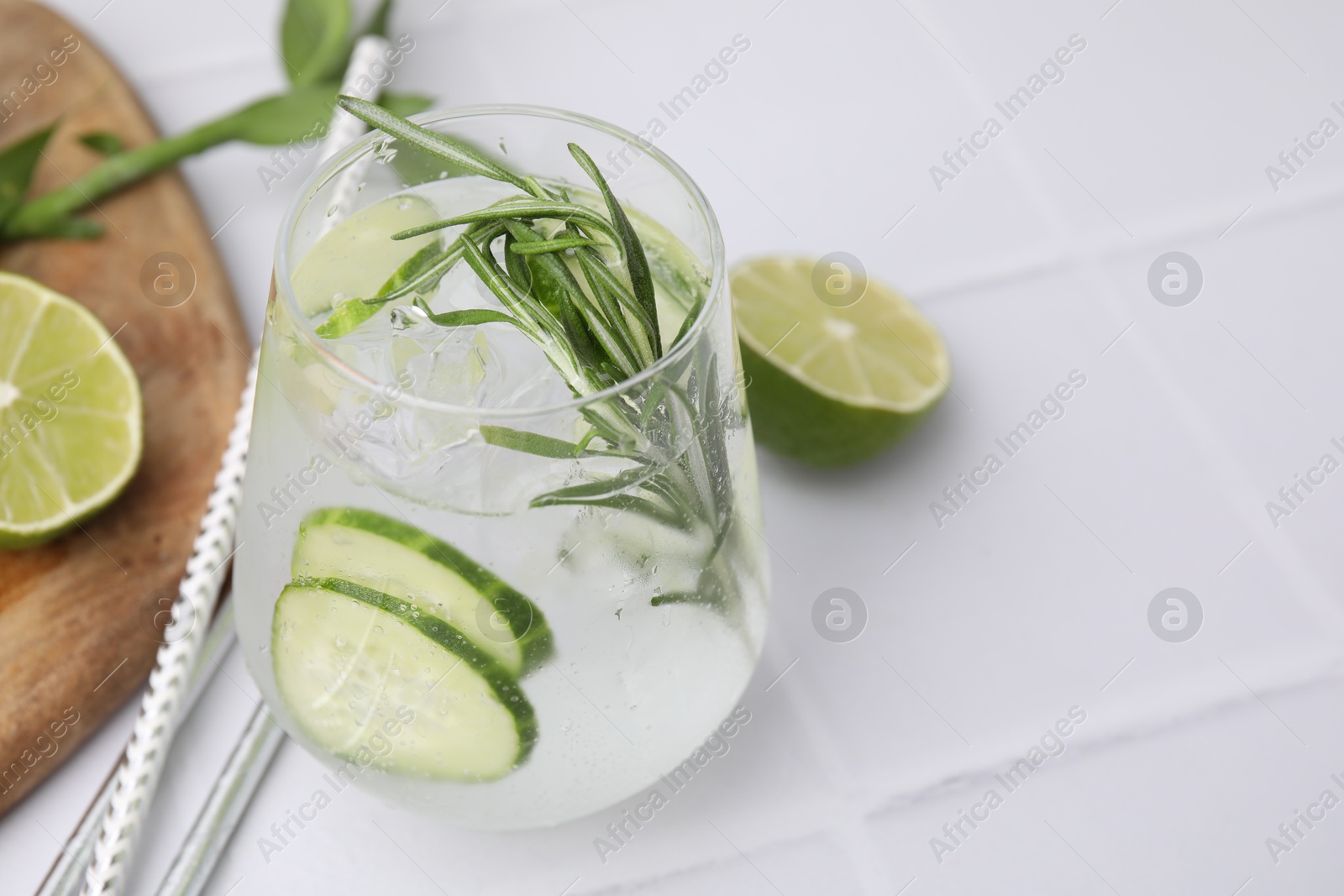 Photo of Refreshing water with cucumber and rosemary in glass on white tiled table, closeup. Space for text