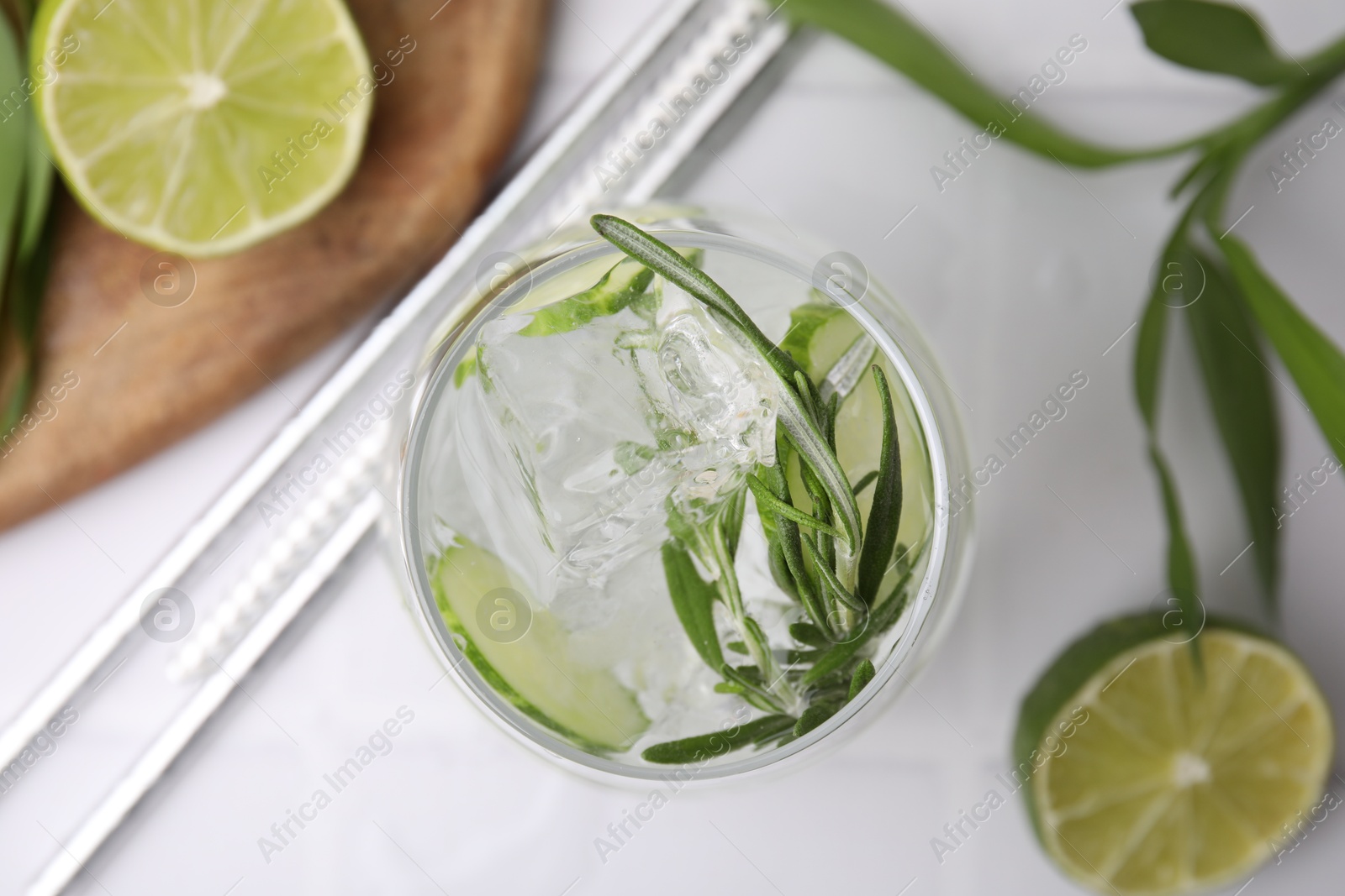 Photo of Refreshing water with cucumber and rosemary in glass on white tiled table, flat lay