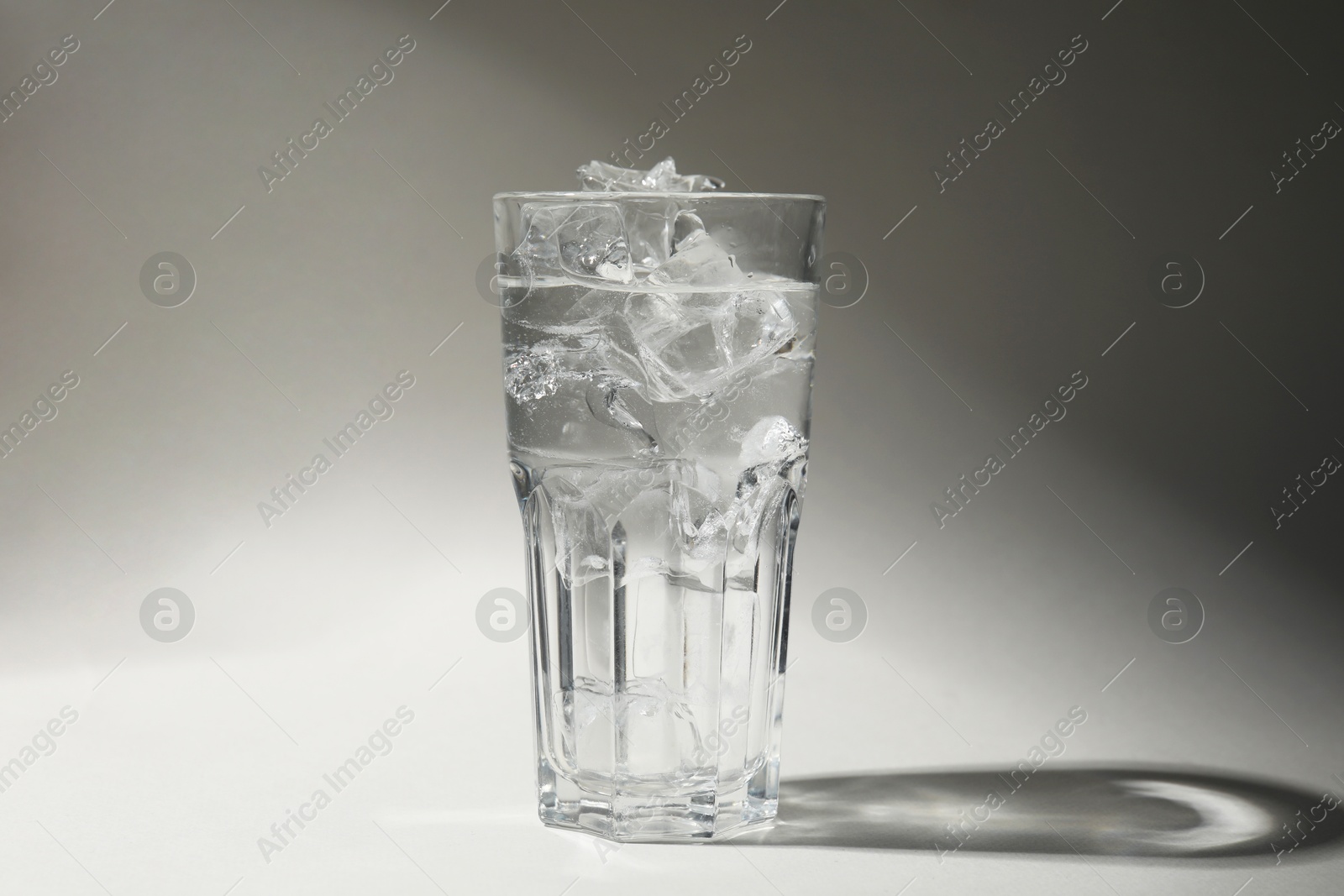 Photo of Refreshing water with ice in glass on grey background