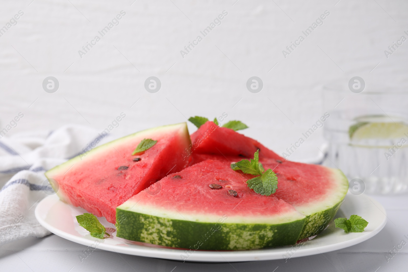 Photo of Fresh watermelon slices with mint leaves on white tiled table, closeup