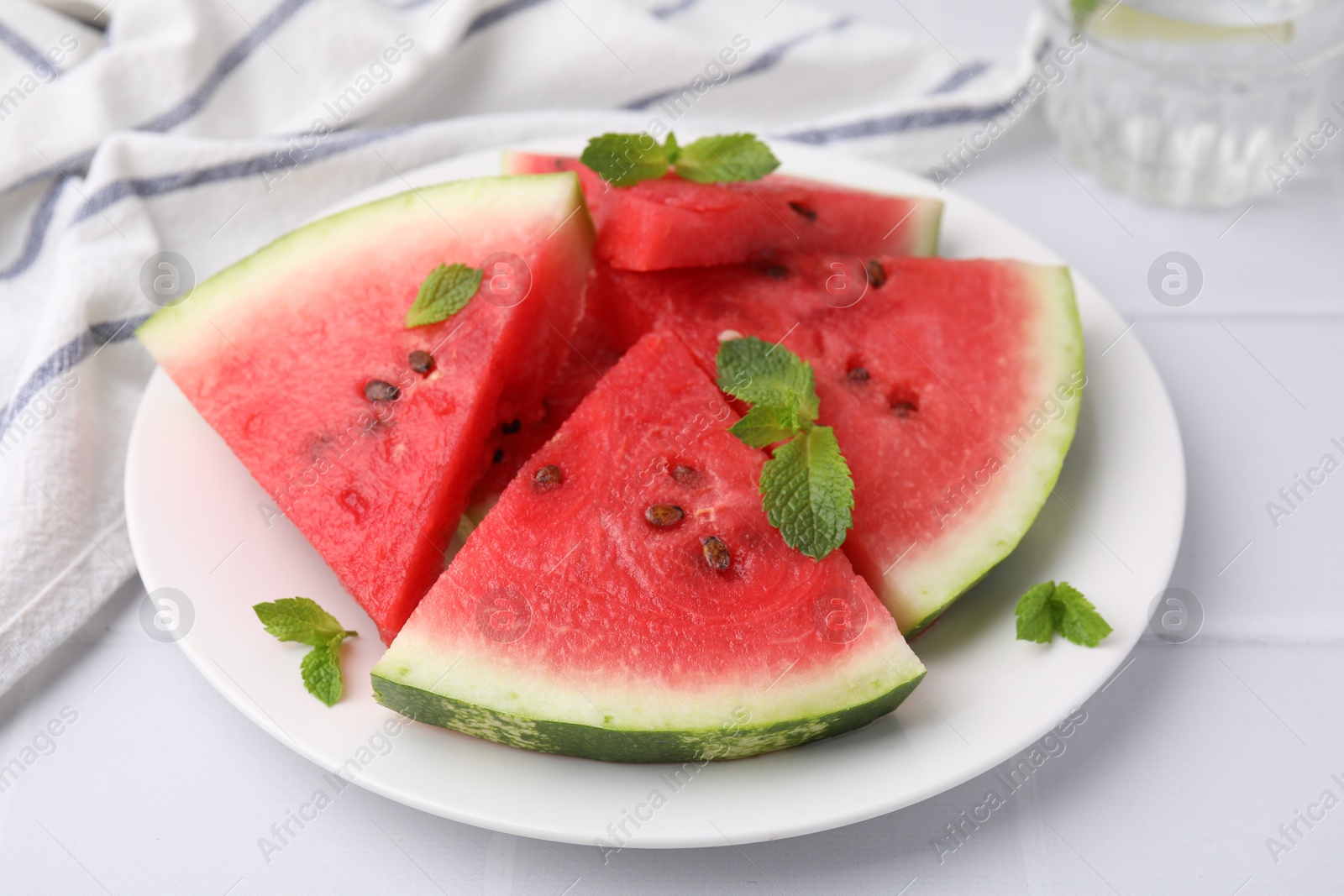 Photo of Fresh watermelon slices with mint leaves on white tiled table, closeup