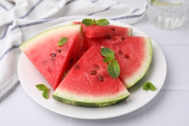 Photo of Fresh watermelon slices with mint leaves on white tiled table, closeup