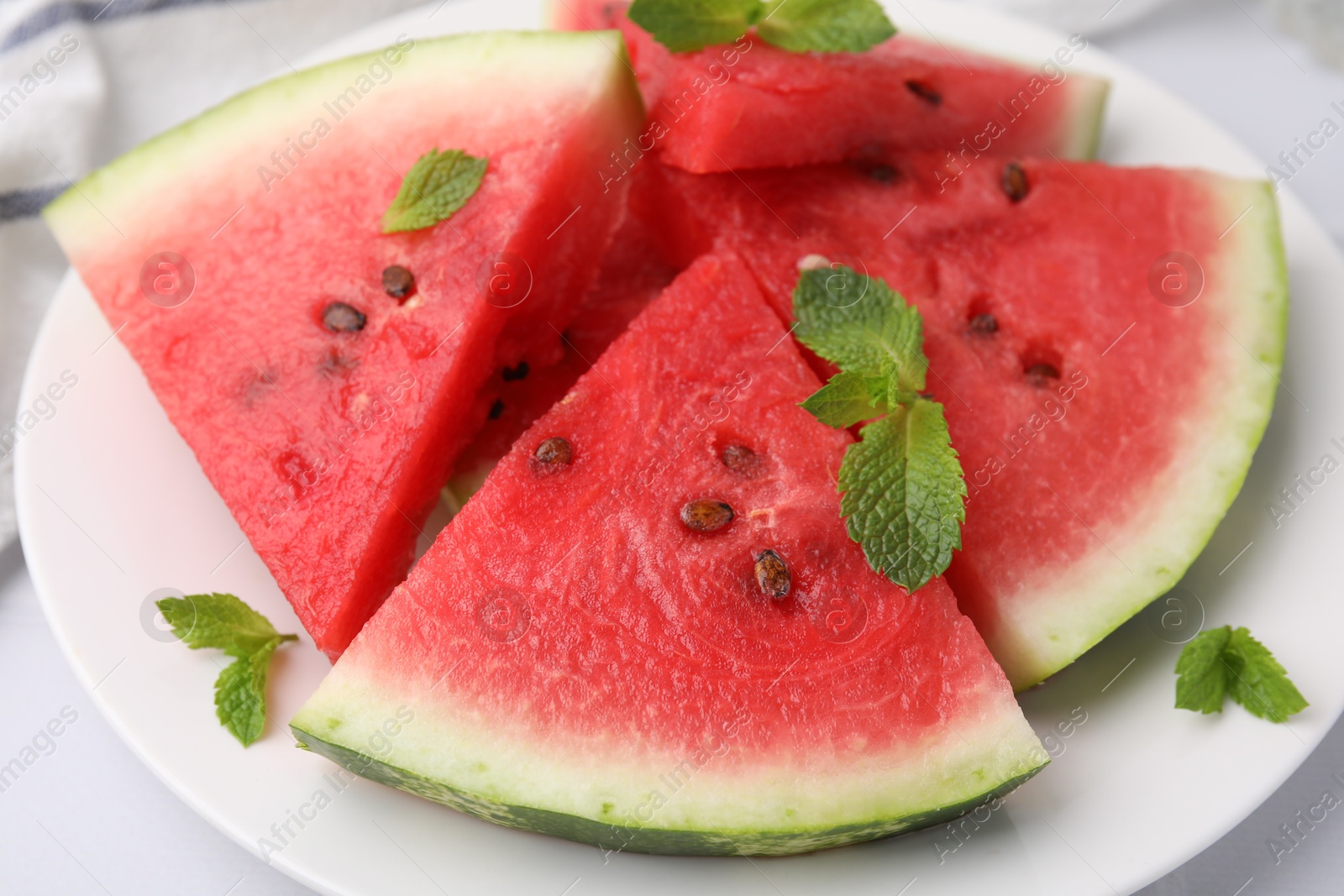 Photo of Fresh watermelon slices with mint leaves on white table, closeup