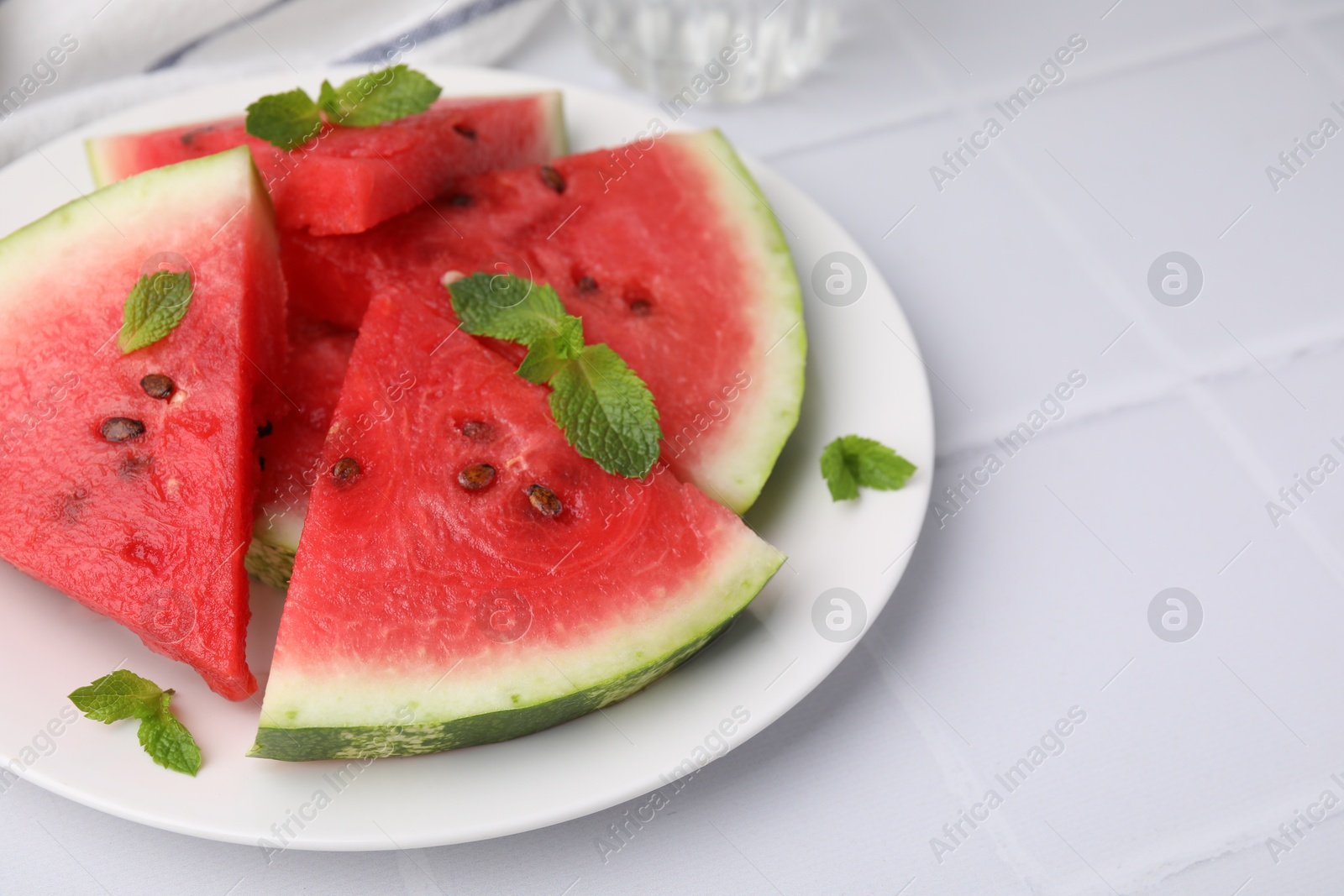 Photo of Fresh watermelon slices with mint leaves on white tiled table, closeup. Space for text