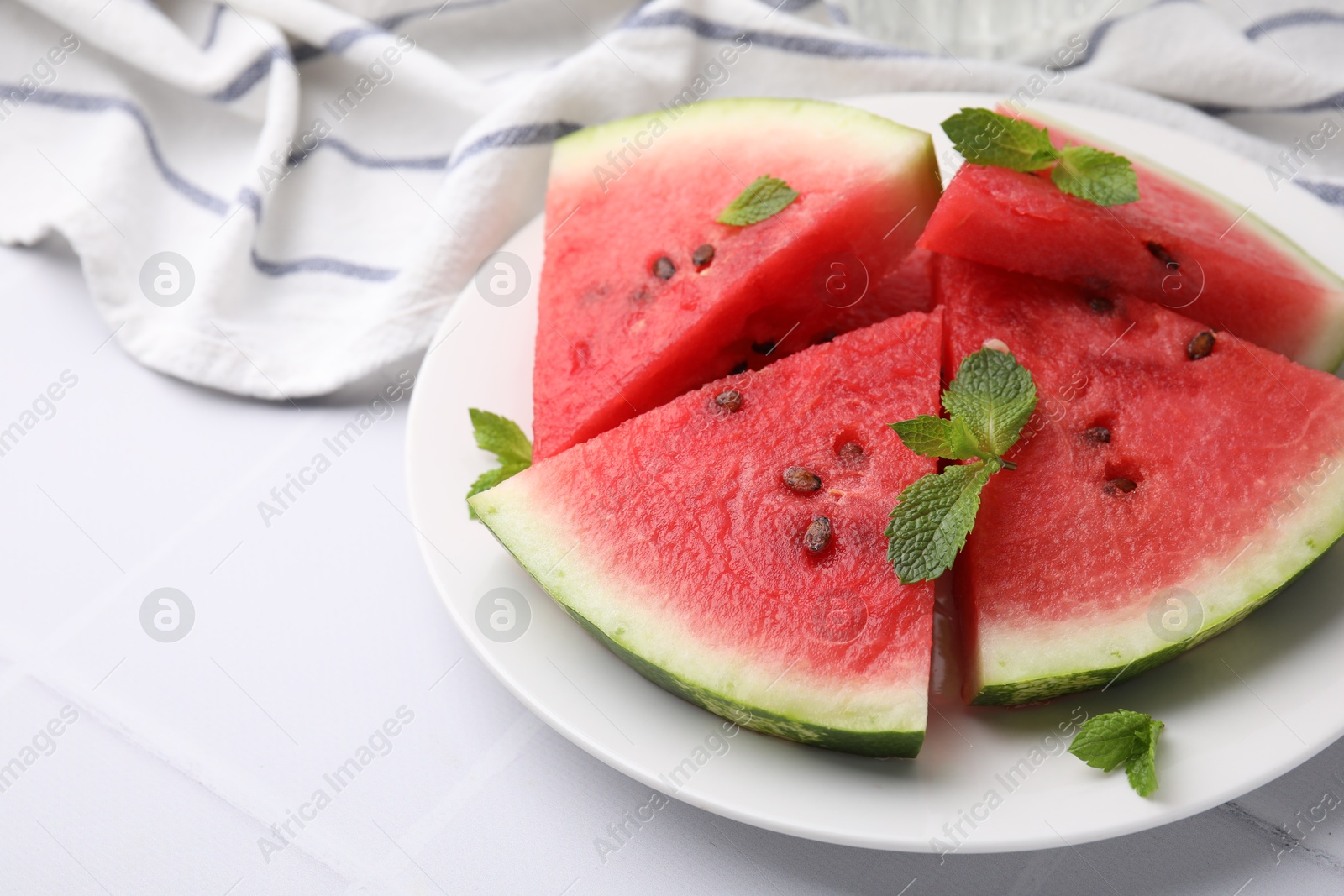 Photo of Fresh watermelon slices with mint leaves on white tiled table, closeup. Space for text