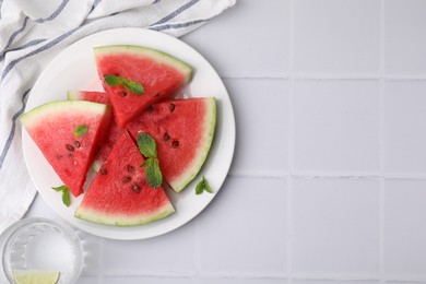 Photo of Fresh watermelon slices with mint and glass of water on white tiled table, flat lay. Space for text