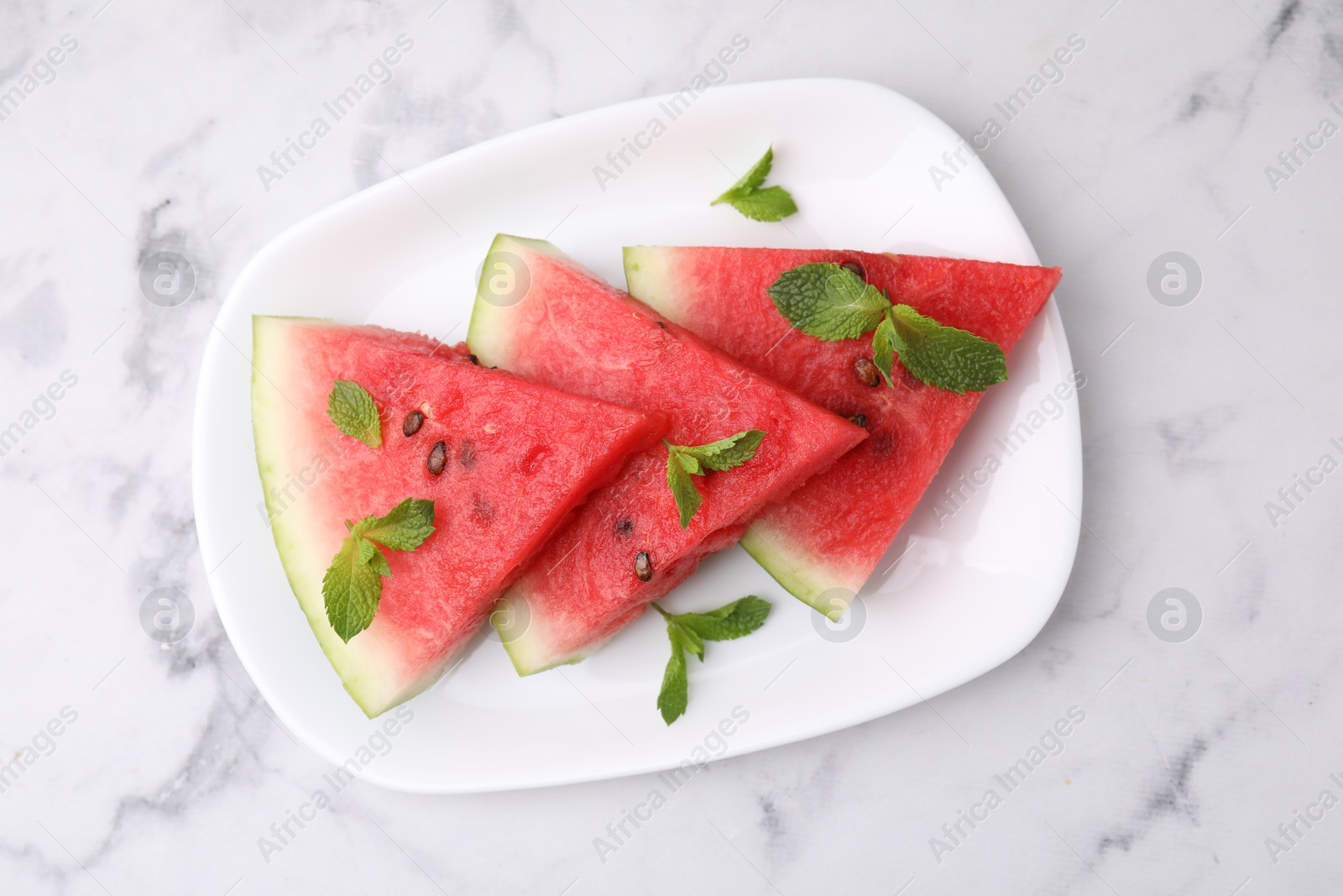 Photo of Fresh watermelon slices with mint leaves on white marble table, top view