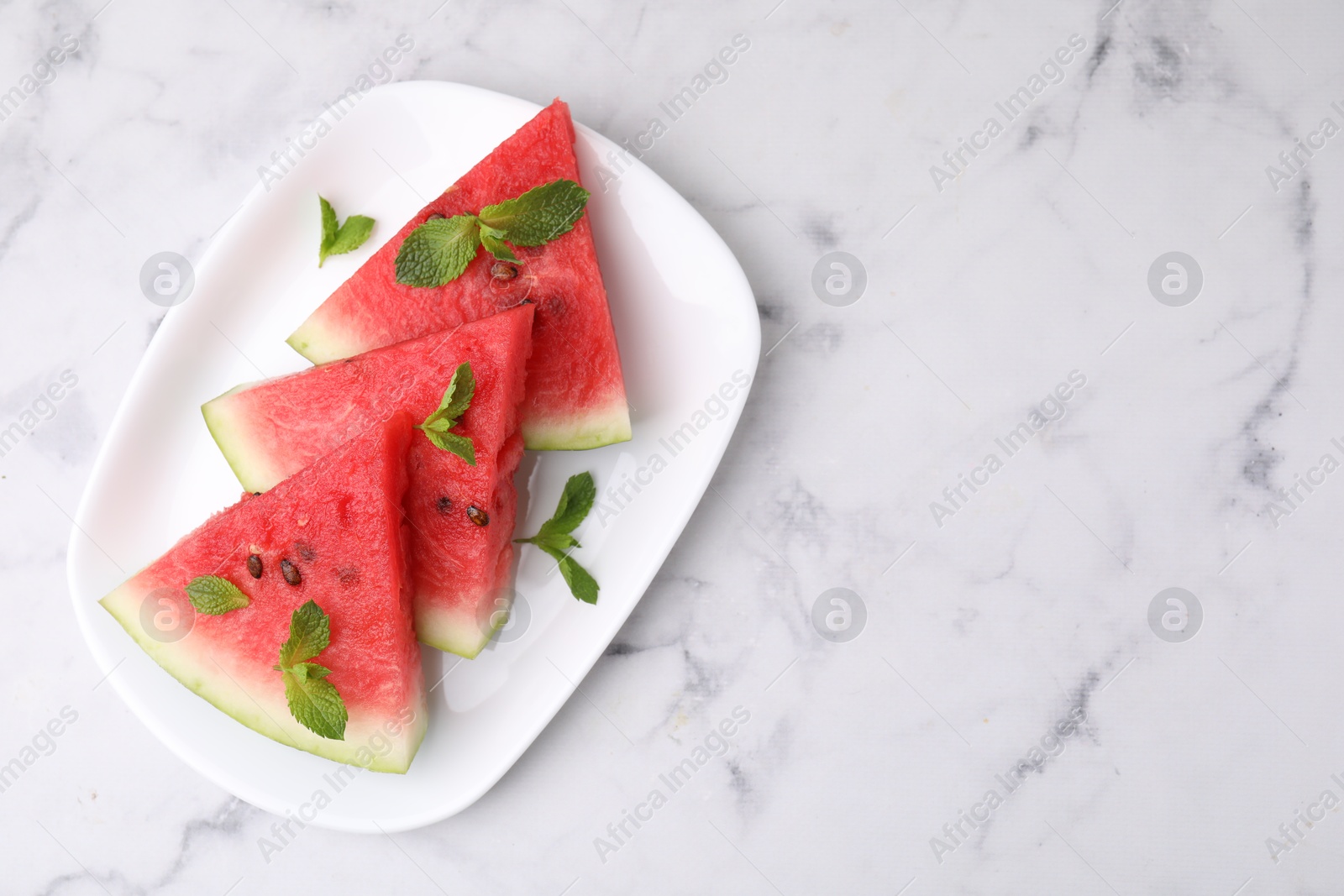 Photo of Fresh watermelon slices with mint leaves on white marble table, top view. Space for text