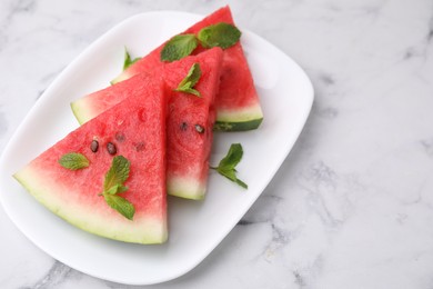 Photo of Fresh watermelon slices with mint leaves on white marble table, closeup. Space for text