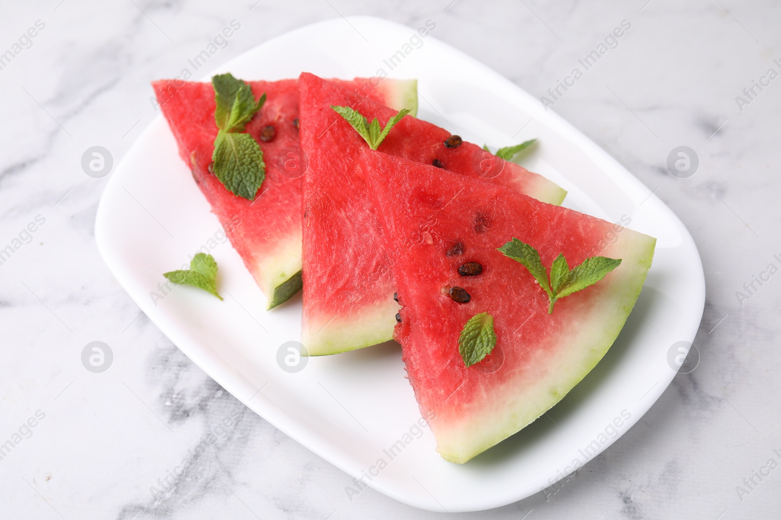 Photo of Fresh watermelon slices with mint leaves on white marble table, closeup