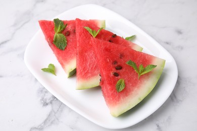 Fresh watermelon slices with mint leaves on white marble table, closeup