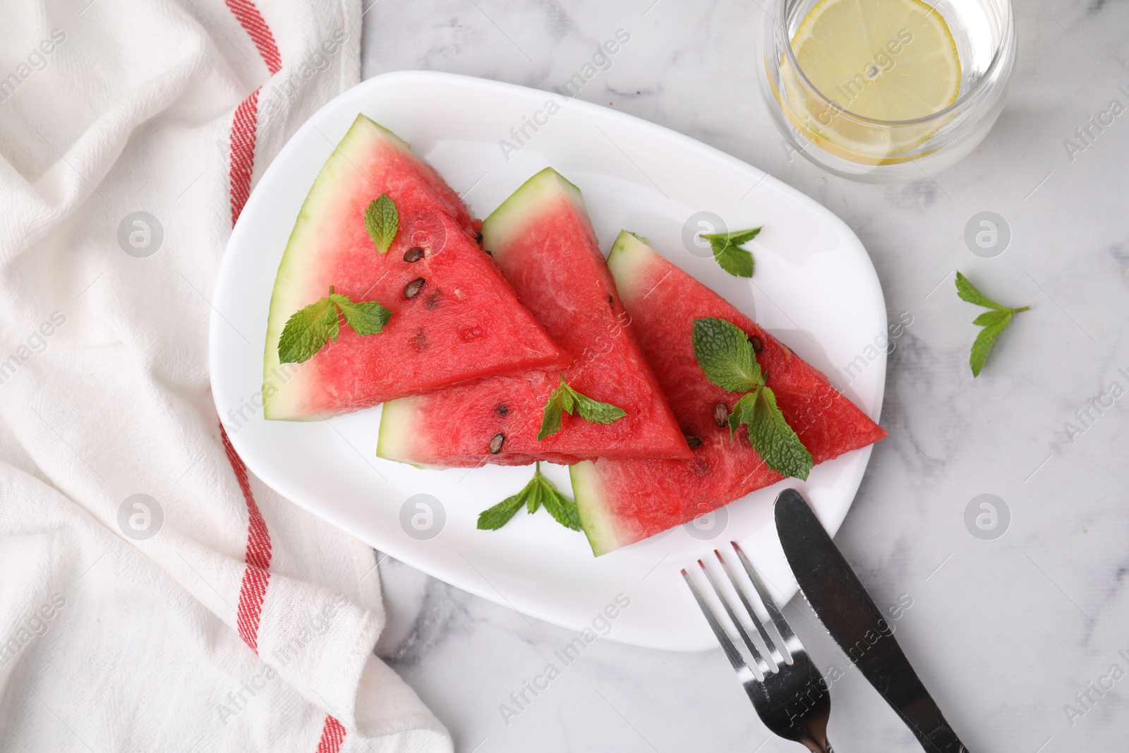 Photo of Fresh watermelon slices with mint leaves and glass of water on white marble table, flat lay