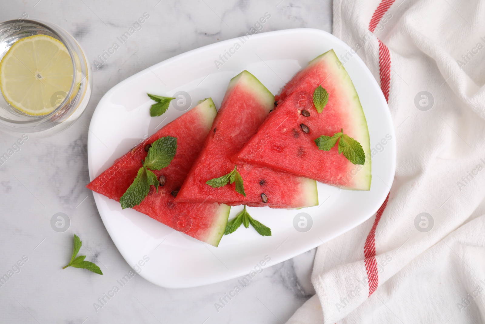 Photo of Fresh watermelon slices with mint leaves and glass of water on white marble table, flat lay