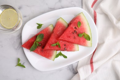 Photo of Fresh watermelon slices with mint leaves and glass of water on white marble table, flat lay