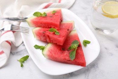 Photo of Fresh watermelon slices with mint leaves and glass of water on white marble table, closeup