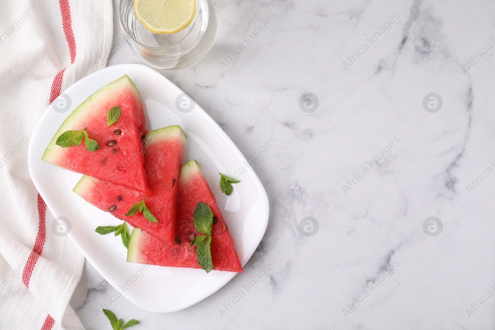 Photo of Fresh watermelon slices with mint and glass of water on white marble table, flat lay. Space for text