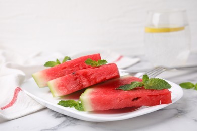 Photo of Fresh watermelon slices with mint leaves on white marble table, closeup