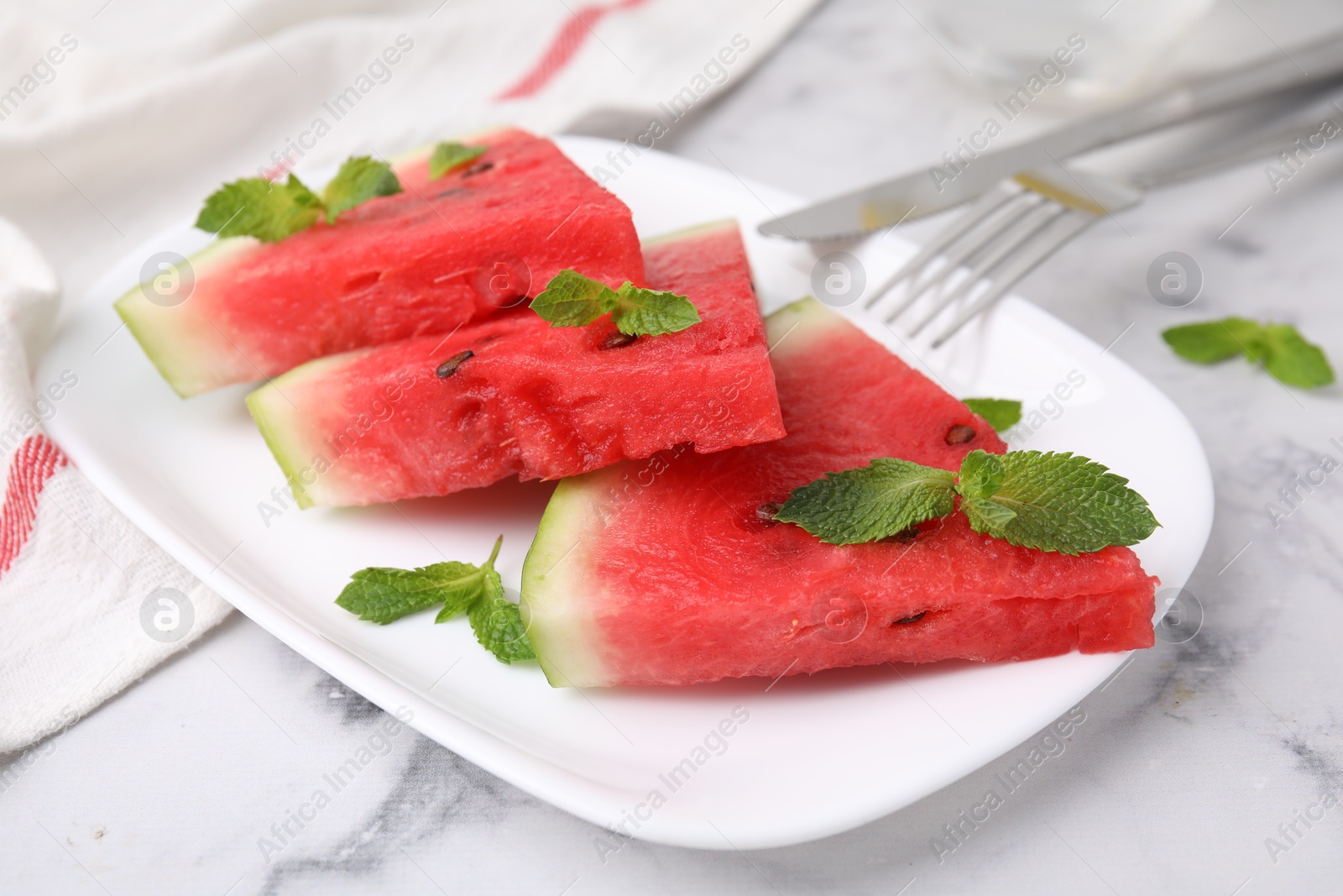 Photo of Fresh watermelon slices with mint leaves on white marble table, closeup