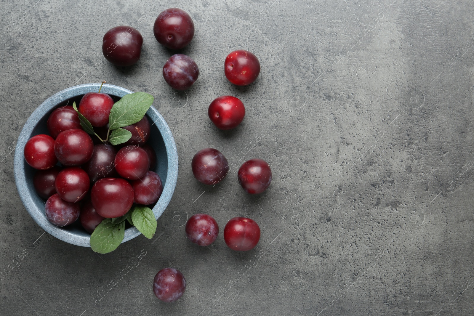 Photo of Fresh plums on grey textured table, flat lay. Space for text