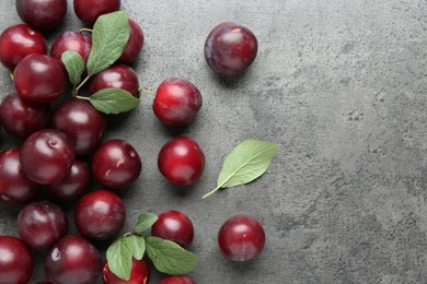 Photo of Fresh plums and leaves on grey textured table, flat lay. Space for text