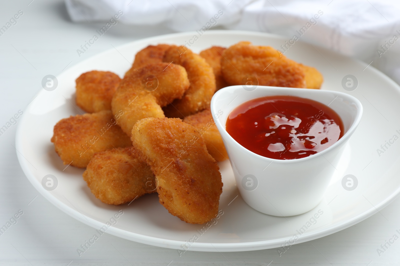 Photo of Tasty chicken nuggets with chili sauce on white table, closeup