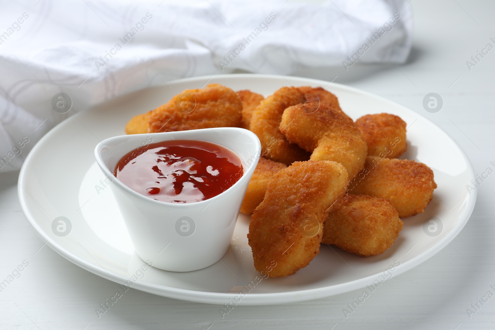 Photo of Tasty chicken nuggets with chili sauce on white table, closeup