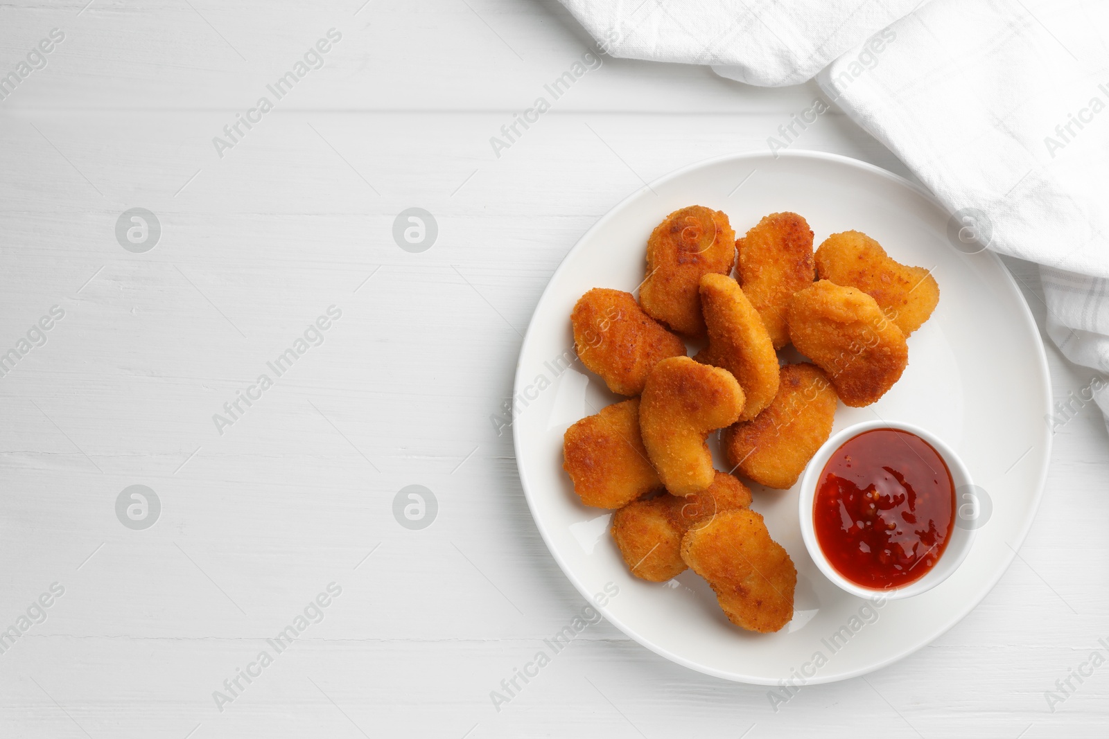 Photo of Tasty chicken nuggets with chili sauce on white wooden table, top view. Space for text