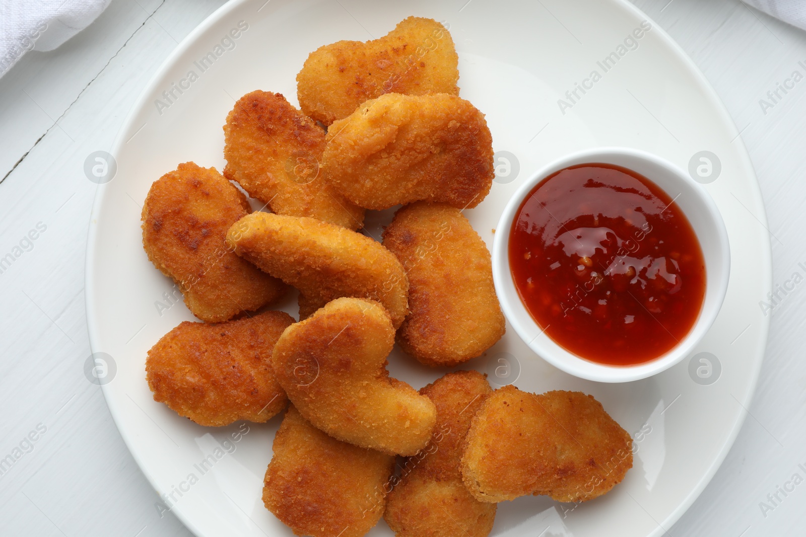 Photo of Tasty chicken nuggets with chili sauce on white table, top view