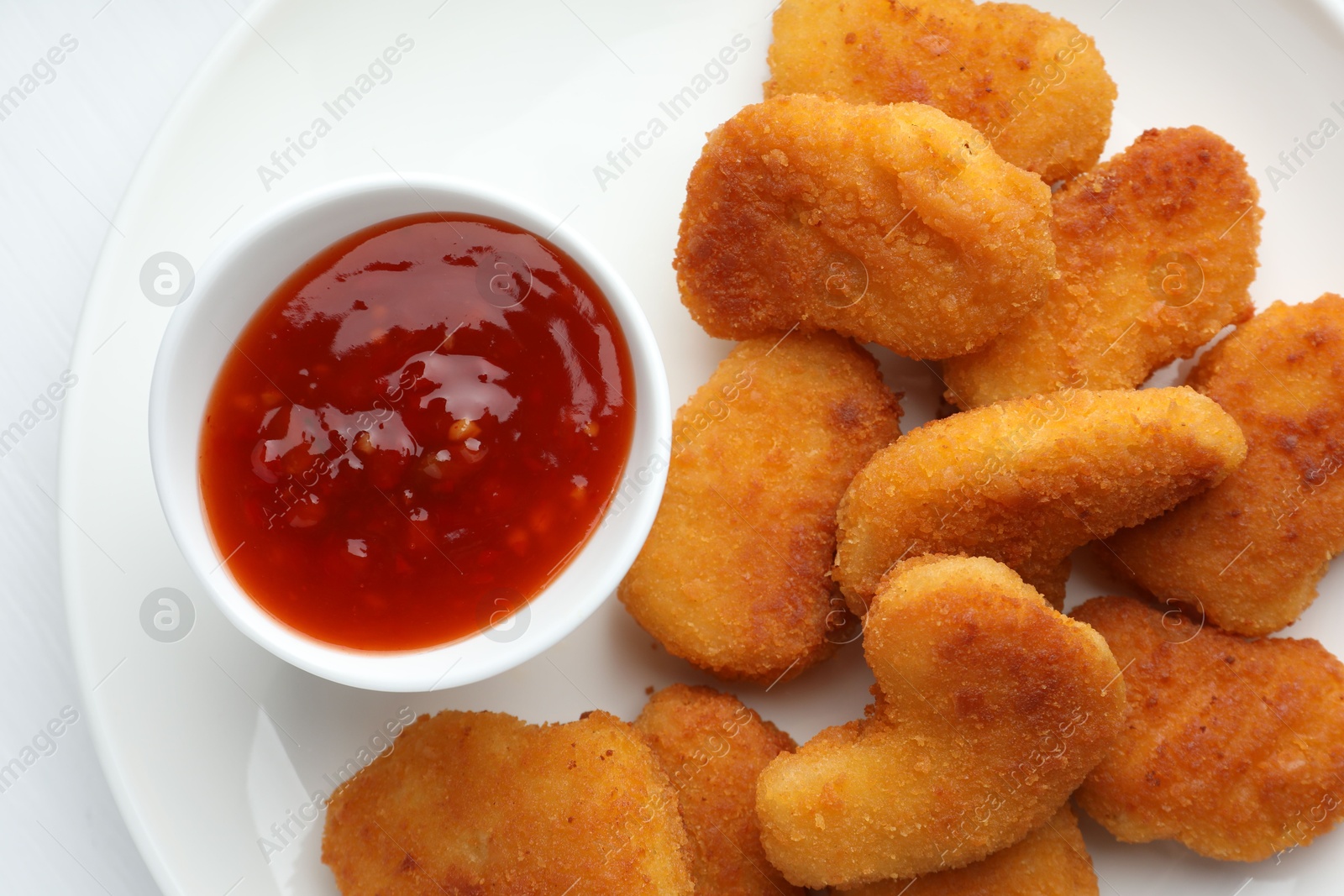 Photo of Tasty chicken nuggets with chili sauce on white table, flat lay