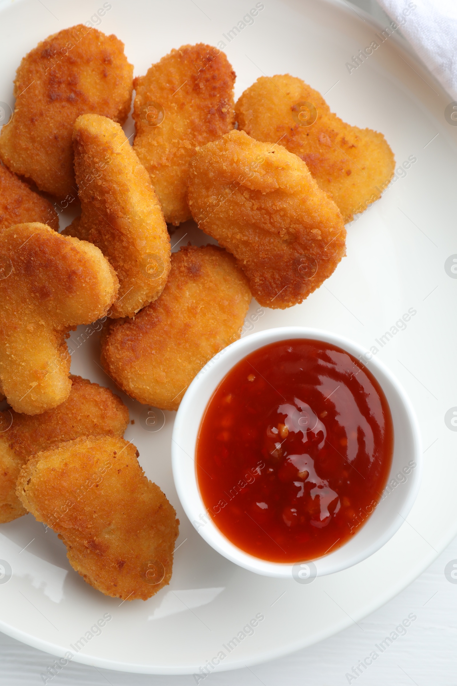 Photo of Tasty chicken nuggets with chili sauce on white table, flat lay