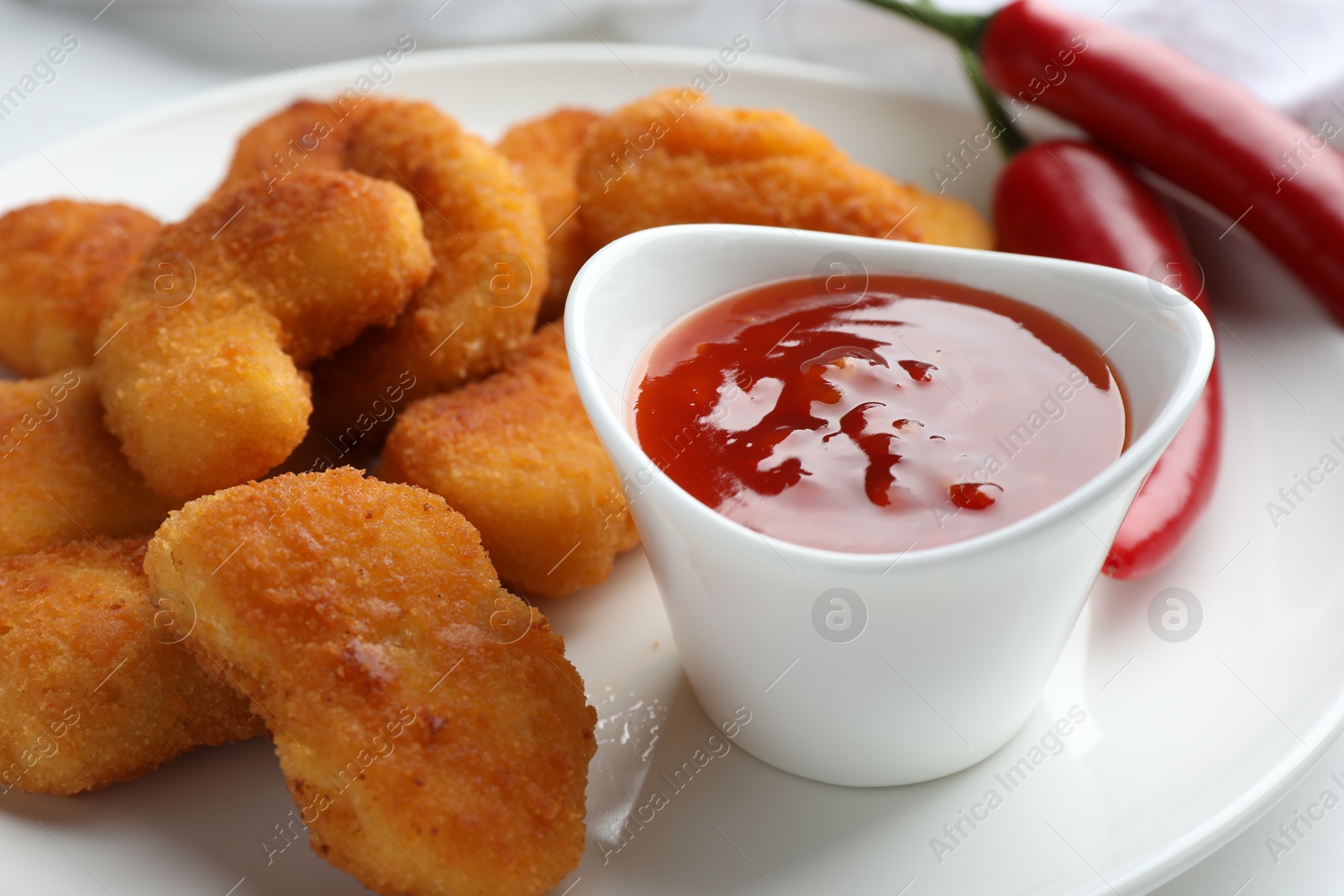 Photo of Tasty chicken nuggets with chili sauce on white table, closeup