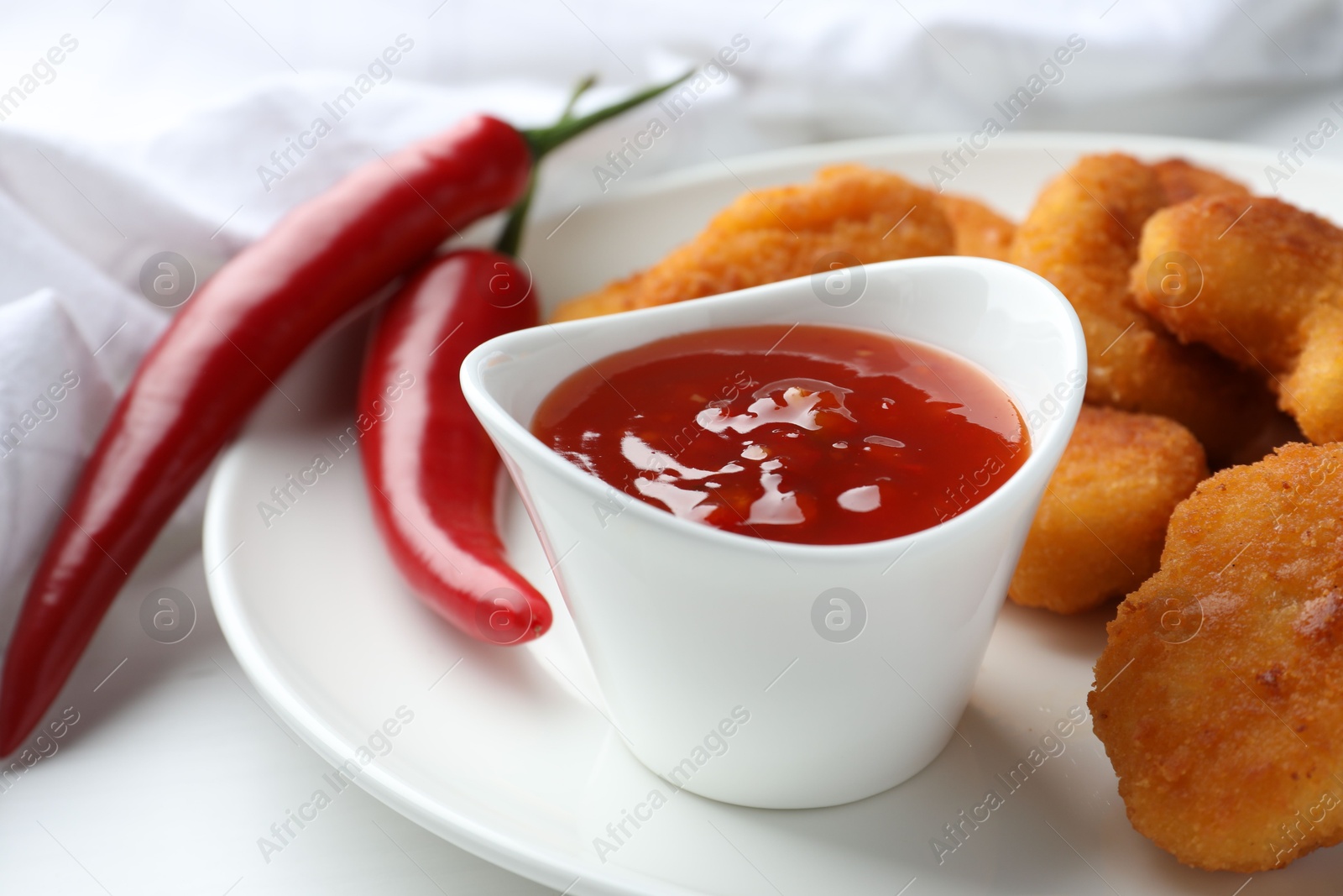 Photo of Tasty chicken nuggets with chili sauce on white table, closeup