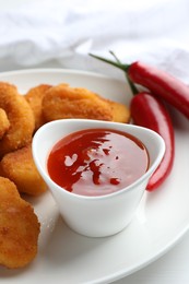 Photo of Chili sauce and chicken nuggets on white table, closeup