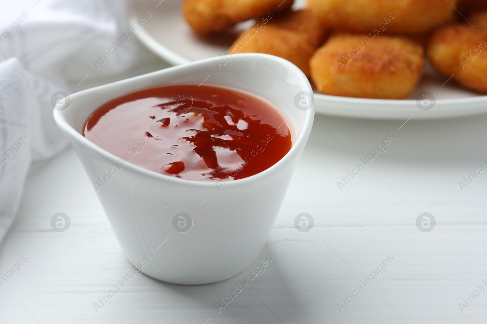 Photo of Spicy chili sauce in bowl on white wooden table, closeup