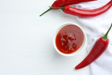 Photo of Spicy chili sauce in bowl and fresh peppers on white wooden table, flat lay. Space for text