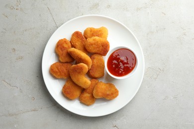 Photo of Tasty chicken nuggets with chili sauce on grey textured table, top view