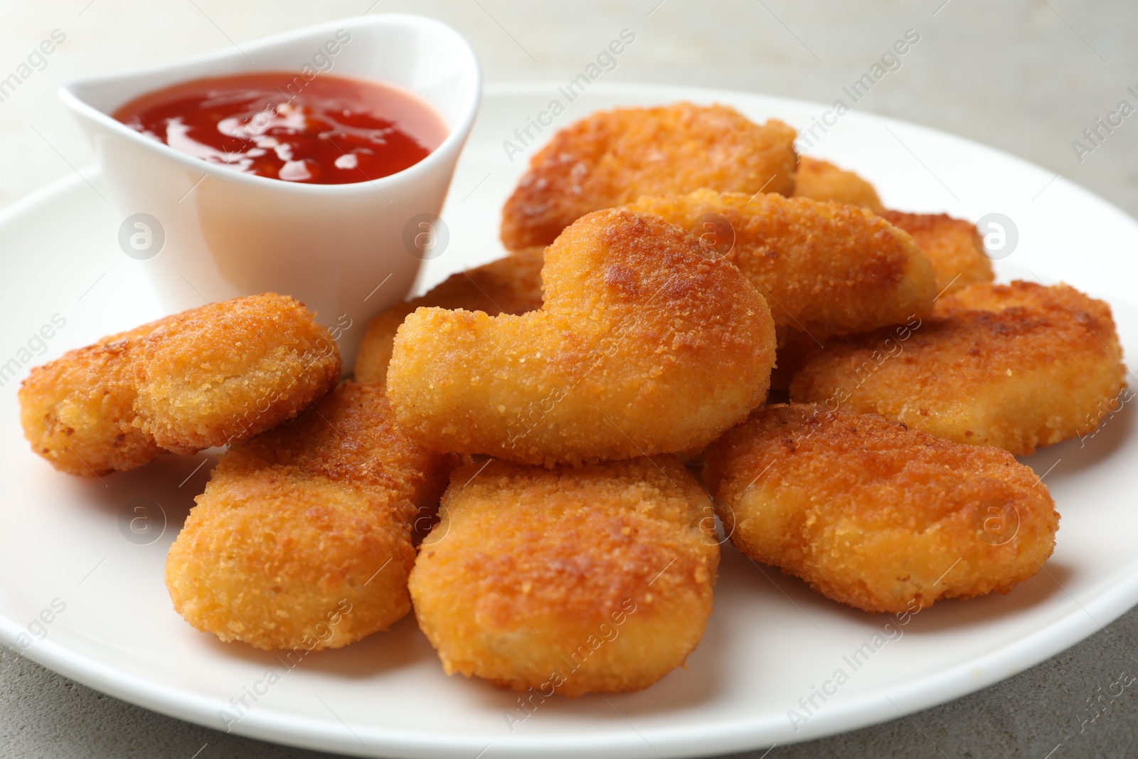 Photo of Tasty chicken nuggets with chili sauce on grey table, closeup