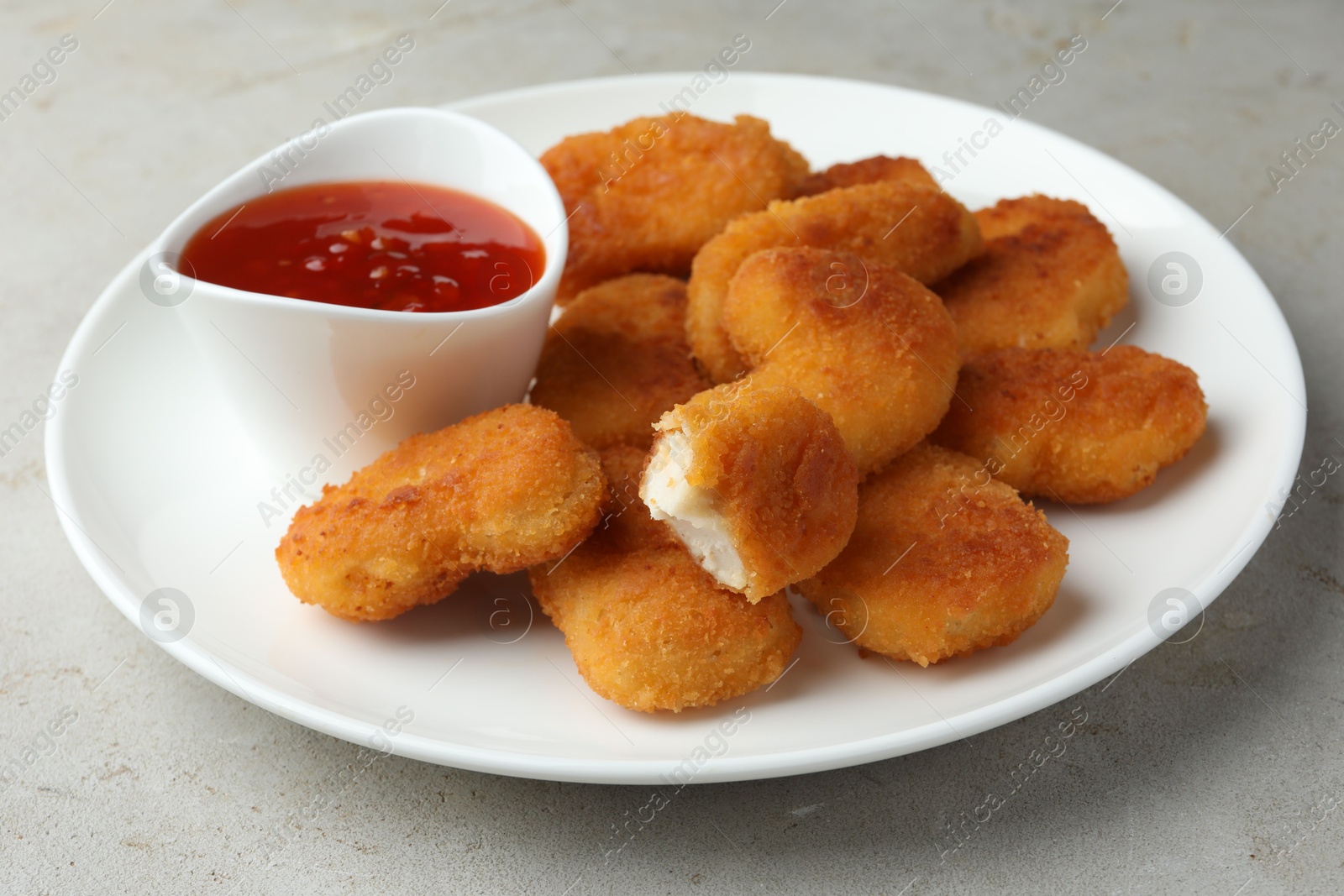 Photo of Tasty chicken nuggets with chili sauce on grey textured table